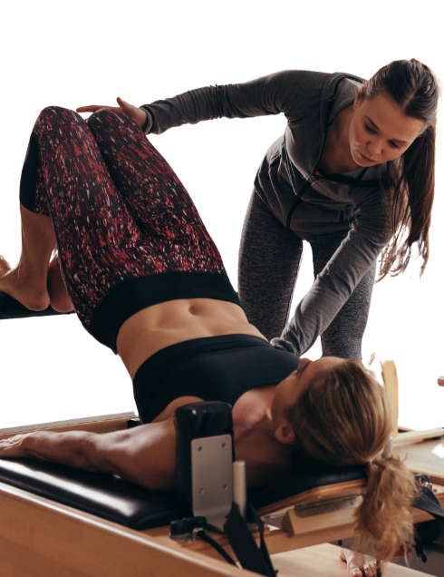 Pilates instructor guiding a client on a reformer machine, demonstrating proper form and technique in a studio setting.
