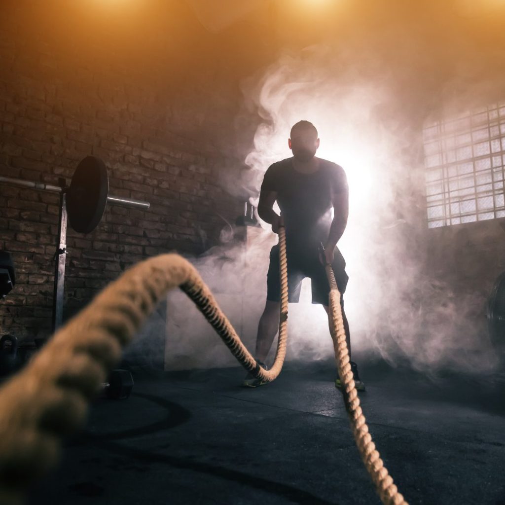 Personal trainer using battle ropes in a gym, emphasizing fitness coaching intensity and need for liability insurance.