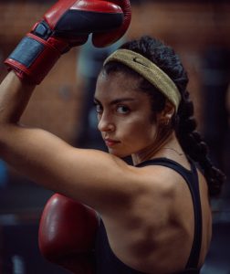 A focused woman wearing boxing gloves in a gym, symbolizing determination and strength, key traits for running a successful personal training business from home.