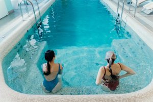Two women in swimsuits engaging in a relaxing aquatic exercise session in a pool, ideal for low-impact senior workouts.