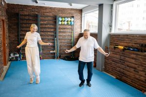A senior couple smiling and skipping rope together in a gym, enjoying a fun and energetic workout.